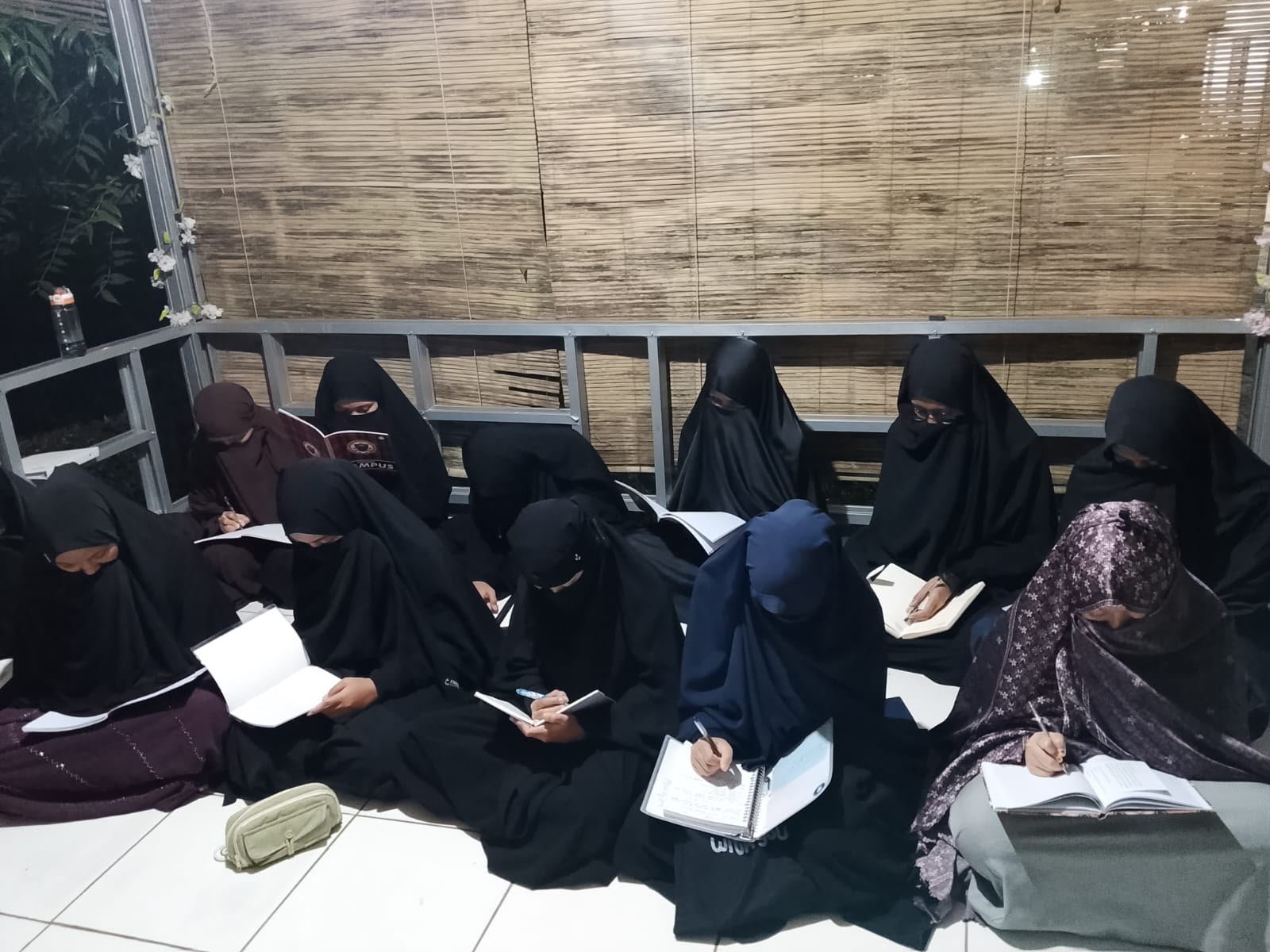 Santriwati duduk melingkar di atas lantai sambil membaca mushaf pada kegiatan halaqah