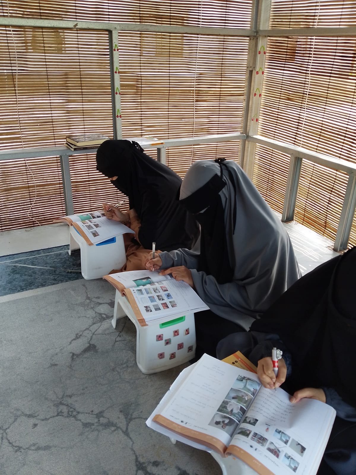 Seorang ustadzah menyimak bacaan santriwati dari dekat di meja kecil
