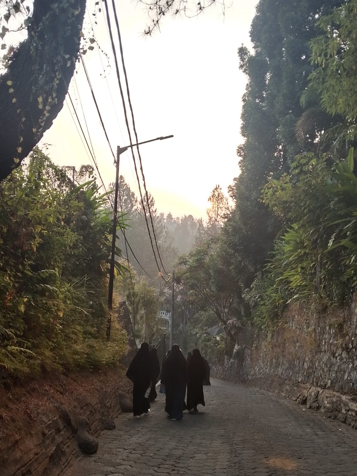 Santriwati berjalan menyusuri jalan menuju kegiatan pagi di tengah kabut