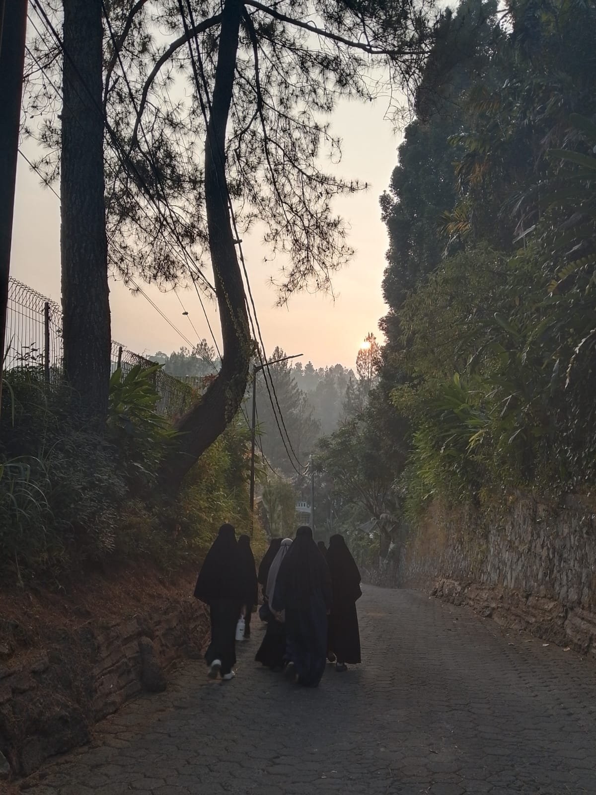 Beberapa santriwati berjalan menyusuri jalan kampung yang masih berkabut pada pagi hari di Megamendung